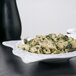 A white Las Brisas square melamine bowl filled with pasta and spinach.