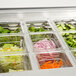 A salad bar with different vegetables in clear plastic containers.