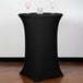 A black Snap Drape bar height spandex table cover on a round table with wine glasses on it.