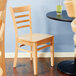 A Lancaster Table & Seating wooden chair with natural wood seat next to a table.