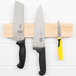 A Mercer Culinary rubberwood magnetic knife holder with three knives on it.