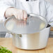 A chef using a Vollrath Wear-Ever domed aluminum pot cover to cook vegetables.