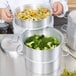 A chef uses a Vollrath 3-tier vegetable steamer to cook broccoli in a large metal pot.