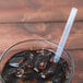 A glass with a straw in it filled with brown liquid and ice.