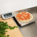 An Edlund digital pizza scale on a table next to a pepperoni pizza.