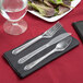 A Hoffmaster black linen-like napkin pre-rolled with clear plastic fork, spoon, and knife.