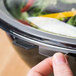 A person using a Fineline clear plastic flat lid to cover a bowl of salad.