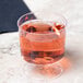 A Visions heavy weight clear plastic wine glass filled with pink liquid on a marble counter.