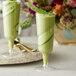 Two Visions plastic champagne flutes filled with green cucumber smoothies and garnished with cucumber slices.