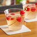 Two clear plastic cups with raspberry drinks and fruit on a table.