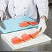 A chef cutting raw salmon on a white surface with a knife.