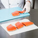 A person cutting raw salmon on a white cutting board.