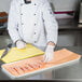 A chef cutting raw chicken on a yellow cutting board using a knife.