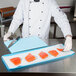 A chef cutting raw salmon on a white surface with a black knife on a blue cutting board.