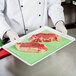 A chef holding a tray of raw meat on green steak paper.