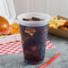 A Dart translucent plastic cup filled with soda and ice on a table with a sandwich and chicken.