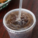 A Solo clear PET lid with a straw slot on a plastic cup with a straw.
