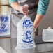 A man in a blue apron holding a clear plastic bag with an ice print on it.