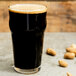 A Libbey English Pub glass filled with dark beer on a table with peanuts.