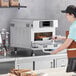 A woman wearing gloves prepares a pizza in a white TurboChef Bullet oven.