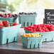 A group of green molded pulp baskets holding strawberries and berries on a table.
