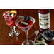 A glass of red liquid with blackberries and a bottle of Monin Premium Blackberry Fruit Syrup on a table.