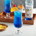 A blue drink with a slice of orange on top in a blue glass with a white label on the bottle of Monin Premium Blue Curacao Flavoring Syrup.