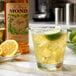 A glass of Monin Organic Agave Nectar Sweetener with a drink and a lime slice on a marble counter.