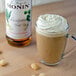 A glass cup of coffee with Monin Macadamia Nut Syrup-flavored whipped cream and nuts.