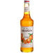 A Monin bottle of orange syrup with orange liquid inside.