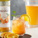 A glass of Monin orange drink with ice and orange slices on a table.