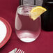 A Libbey stemless wine glass filled with water and a lemon wedge on a table with a red tablecloth.