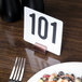 An American Metalcraft hammered copper table card holder with a number on a table next to a plate of food.