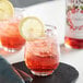 A glass of red liquid with a slice of Monin Premium Cranberry Fruit Syrup on a table with a lemon slice on top.