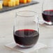 Two customizable Acopa stemless wine glasses filled with red wine on a table.