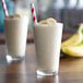 Two glasses of Monin banana smoothie with straws and bananas.