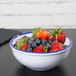 A Cal-Mil white melamine bowl with a blue rim filled with strawberries and blueberries.