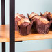 A Cal-Mil rustic pine 3-shelf metal frame riser with muffins on the wooden shelves.