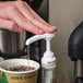 A hand using a Monin syrup pump to pour syrup into a cup of coffee.