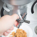 A hand pressing a button to dispense cereal from a Cal-Mil Triple Canister Cereal Dispenser.