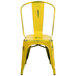 A yellow metal chair with a vertical slat back and drain hole seat.