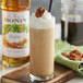 A glass of Monin praline flavoring syrup with whipped cream and pecans.