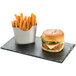 Stainless steel French fry holder with French fries inside on a table with a burger.