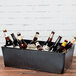 A black Cal-Mil faux slate ice housing container filled with ice and beer bottles on a table.