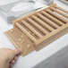 A hand reaching for a wooden Cal-Mil cereal dispenser on a table.