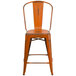 An orange metal restaurant bar stool with a vertical slat back and drain hole seat.