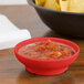 A red salsa dish filled with salsa on a table next to a bowl of chips.