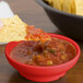 A red melamine salsa bowl with chips on a table.