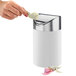 A hand putting a paper into a Cal-Mil white round tabletop trash bin with a stainless steel swing lid.