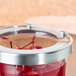 A Cal-Mil Luxe jar filled with red liquid and cherries with a hinged lid.